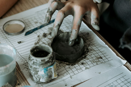 Potter sculpts mug from clay, close up of dirty hands creates vase on white paperの写真素材