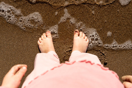 Feet standing on sandy beach with gentle waves washing over the sandの写真素材