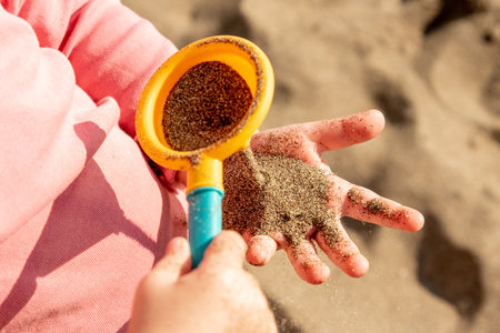 Playing with yellow sand on beach, close up of hand holding sand with orange toy