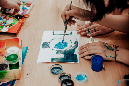 Person painting with watercolors on paper at a table, creating art in an educational setting