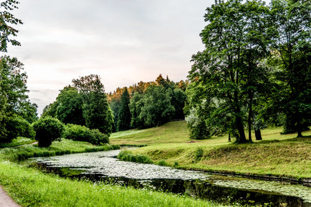 Green city park with walking paths, trail next to a decorative building, cloudy day, Saint...