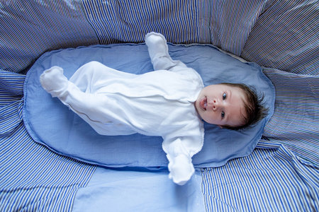Newborn baby lying in crib in bedroom, cute defenseless kid, childhood portrait