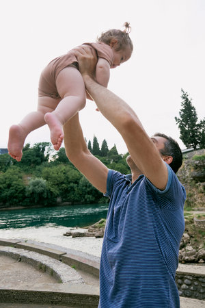 Dad father picks up little cute girl toddler daughter, family activity walk on river beachの写真素材