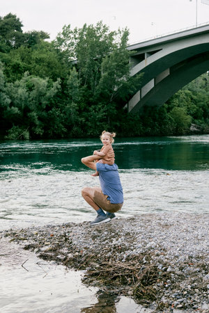 Little cute girl toddler daughter sitting on dad's shoulders, family walking on pebble river beachの写真素材