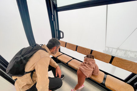 Family father and daughter climbing by cable car, man and girl looking out the window at foggy landscapeの写真素材