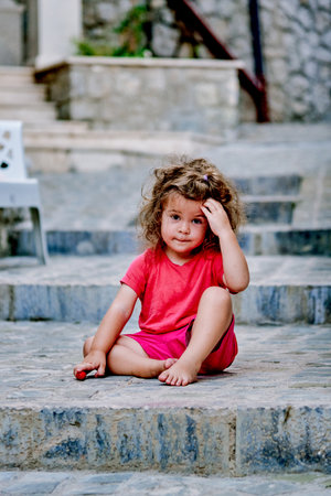 Small thoughtful girl toddler child daughter sitting on stairs outside portrait childhoodの写真素材