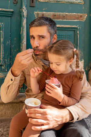 Family man and toddler girl eat ice cream, dad and daughter taste cold fruit dessertの写真素材
