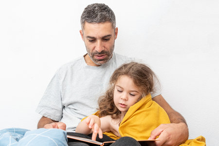 Family man and girl reading children book, dad tells daughter story before going to bedの写真素材