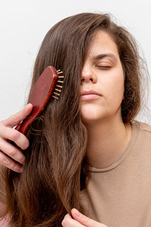 Young woman combining long dark hair with massage comb, daily care routine morningの写真素材