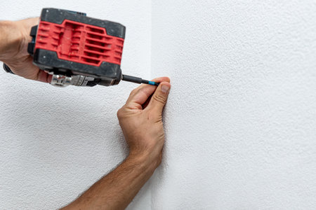 Man repairman makes hole in the wall with drill, repair work in the house with construction equipmentの写真素材