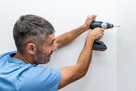 Man repairman makes hole in the wall with drill, repair work in the house with construction equipmentの写真素材