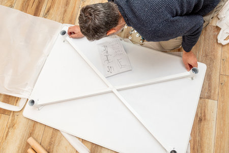 Handyman furniture assembler assembles new wooden dining table with hand screwdriver and screws