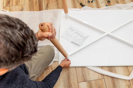 Man handyman furniture assembler assembles new wooden dining table with hand screwdriver and screwsの写真素材
