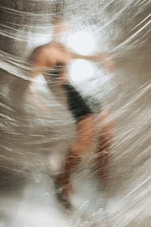 Fashion photo shoot woman model posing behind wet transparent polyethylene membraneの写真素材