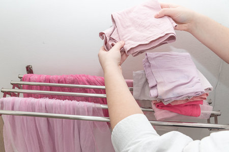 Woman putting pink baby clothes in piles, persona picking up dry clothes from cloth dryer