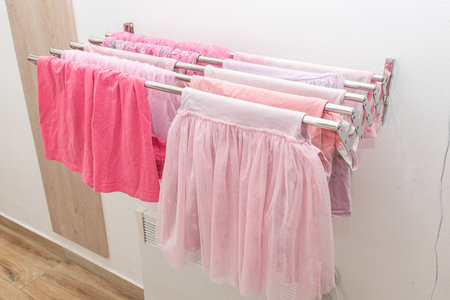 Wet pink child dresses and t-shirts girl hanging on cloth dryers, household chores