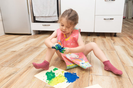 Cute toddler girl child drawing hands with bright colored paints while sitting on the floorの写真素材