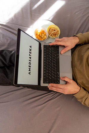 Man watching movie on Amediatheka platform site on laptop while sitting on bed at home