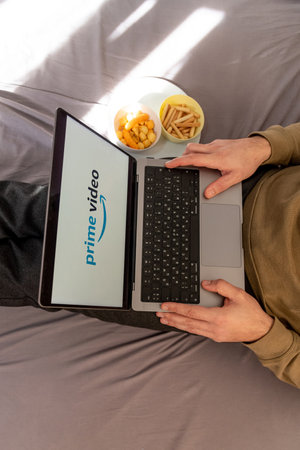 Man watching movie on Prime Video platform site on laptop while sitting on bed at home