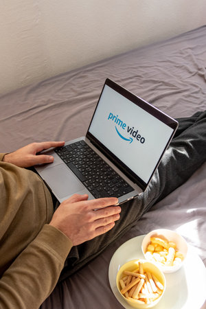 Man watching movie on Prime Video platform site on laptop while sitting on bed at home