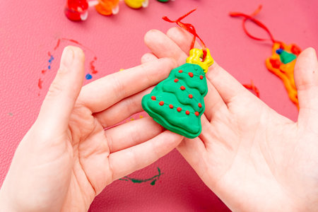 Woman holds in hand and shows DIY handmade gypsum toy Christmas tree painted with color paint