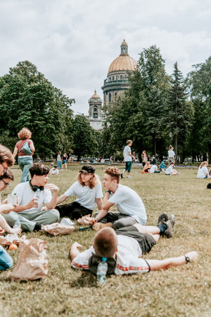 Saint Petersburg, Russia, 2 July 2020, People teenagers on picnic sitting in meadow, St. Isaac's...