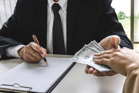 Business woman giving bribe money the form of dollar bills to mature counselor while give success the deal to finishing contract agreement, Bribery and corruption concept.の写真素材
