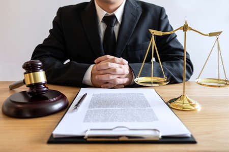 Legal law, advice and justice concept, male lawyer or notary working on a documents and report of the important case and wooden gavel, balance on table in courtroom.の写真素材