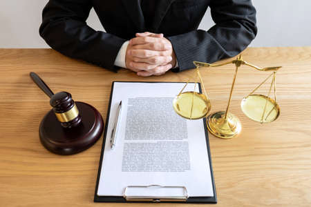 Legal law, advice and justice concept, male lawyer or notary working on a documents and report of the important case and wooden gavel, balance on table in courtroom.の写真素材