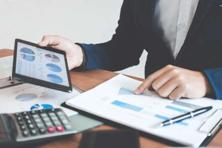Businessman hands using text information on digital tablet to analyze financial statistical chart data and calculate cost of investment project.の写真素材