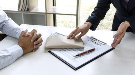 Business woman giving bribe money in a brown envelope while give success the deal to finishing contract agreement, Bribery and corruption concept.の写真素材