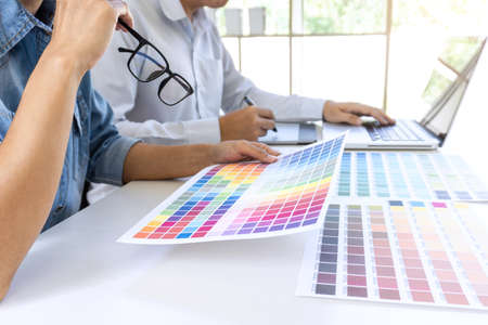 Team of colleague graphic designer drawing and retouching image on graphics tablet and choose color swatch samples for selection on laptop computer.の写真素材