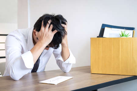 Stressed businessman will being resignation and packing belongings company and files into brown cardboard box, changing and resigning from work concept.の写真素材
