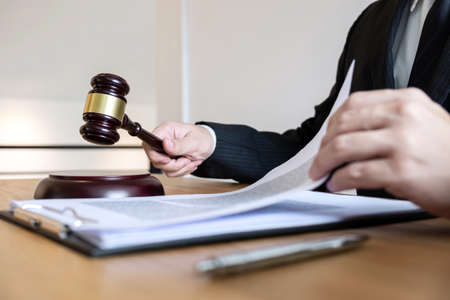 Legal law, advice and justice concept, male counseling lawyer or notary working on a documents and contract papers of the important case and wooden gavel, brass scale in courtroom.の写真素材