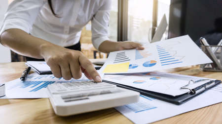 Business woman accountant working and calculating financial data on graph documents, doing finance in workstation.の写真素材