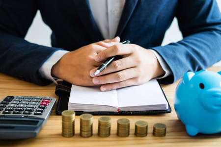 Coin stacks for step up growing business to profit and saving with piggy bank, businessman working with documents and calculator, Saving money for future concept.の写真素材