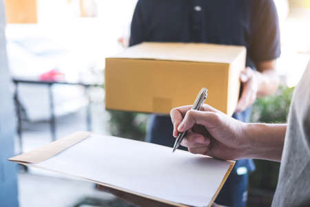 Delivery mail man giving parcel box to recipient and signature form, Young owner signing receipt of...