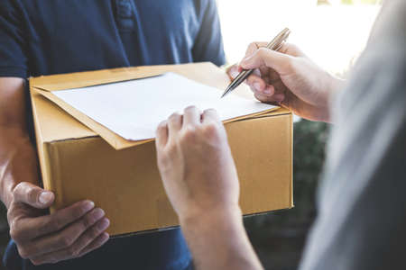 Delivery mail man giving parcel box to recipient and signature form, Young owner signing receipt of...