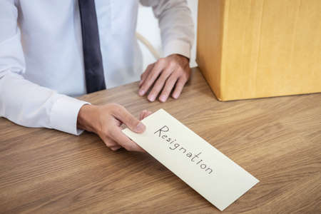 Businessman sending letter will being resignation and carrying packing belongings company and files into brown cardboard box, changing and resigning from work concept.の写真素材