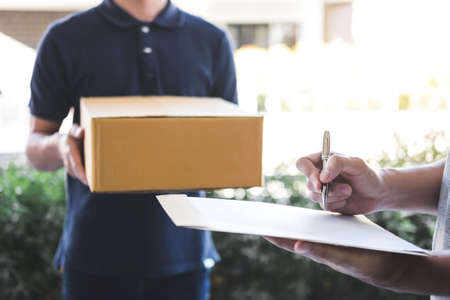 Delivery mail man giving parcel box to recipient, Young man signing receipt of delivery package from...