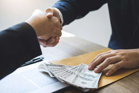 Dishonest cheating in business illegal money, Businessman handshake money of dollar bills in hands from while give success the deal, Bribery and corruption concept.の写真素材