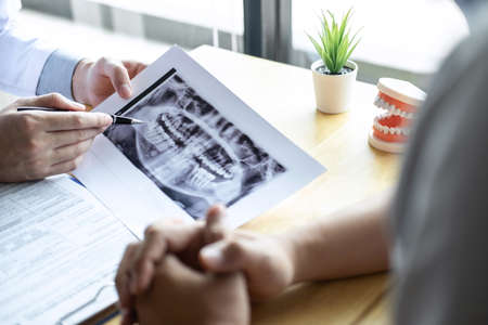 Image of doctor or dentist presenting with tooth x-ray film recommend patient in the treatment of dental and dentistry, working at workplace.の写真素材