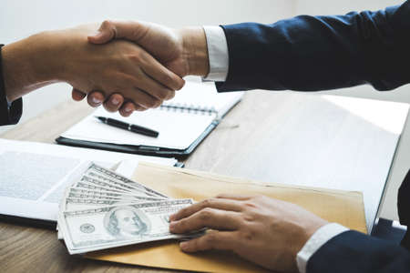 Dishonest cheating in business illegal money, Businessman handshake money of dollar bills in hands from while give success the deal, Bribery and corruption concept.の写真素材