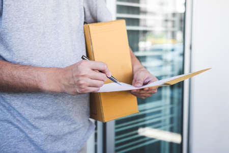 Delivery mail man giving parcel box to recipient, Young man signing receipt of delivery package from post shipment courier at home.の写真素材