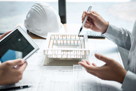 Construction engineering or architect discussing a blueprint and building model while checking...