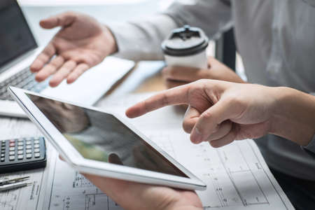 Construction engineering or architect discussing a blueprint and building model while checking...