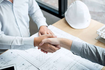 Handshake of collaboration, Construction engineering or architect discuss a blueprint and building model while checking information on sketching, meeting for architectural project of partner.の写真素材