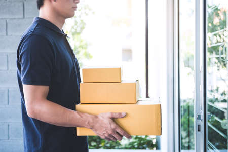 Delivery man standing with parcels in hands outdoors waiting homeowner open door, Home delivery service and working with service mind.の写真素材