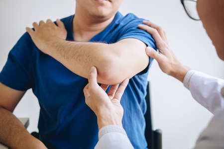 Doctor physiotherapist assisting a male patient while giving exercising treatment massaging the arm...