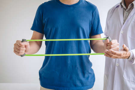 Doctor physiotherapist assisting a male patient while giving exercising treatment on stretching his...